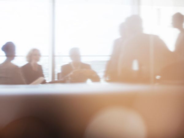 Blurred silhouettes of people in a bright office meeting room. Discussing tax and accounting help.