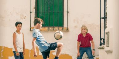 Three boys playing soccer in a narrow street.