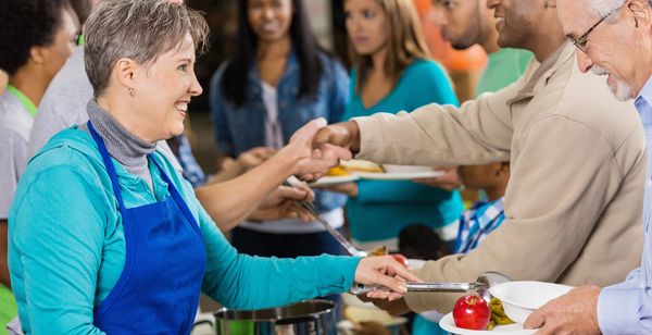 Well-dressed men serving food to a woman in a red polka dot dress at a community event.
