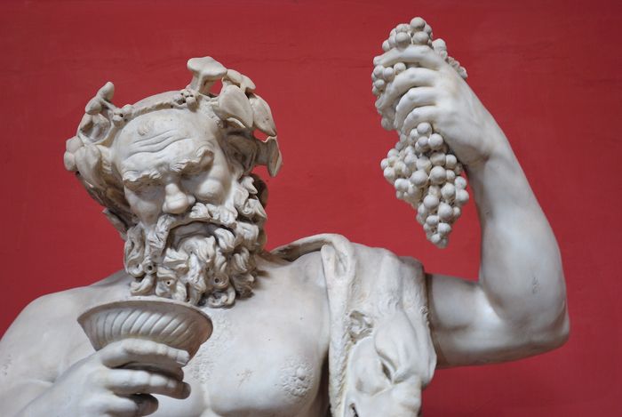 Sculpture of the god Dionysus holding up grabes and looking into a goblet of wine