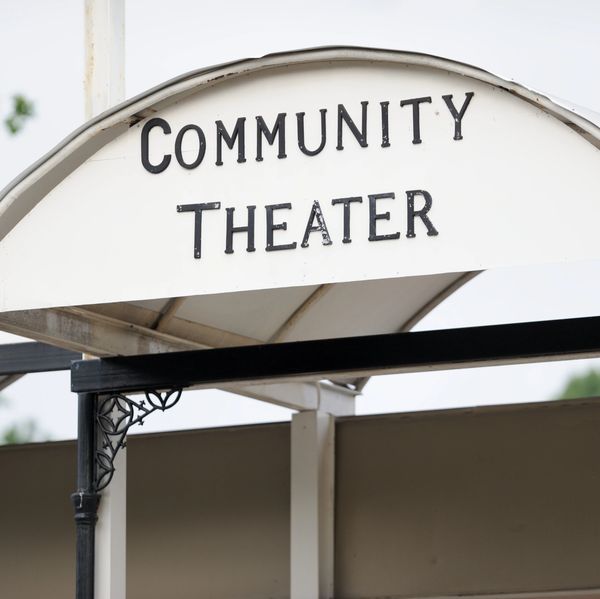 Sign for a community theater with black letters on a white board.