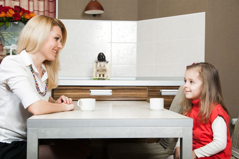 Smiling young mother with daughter drinking tea at the table