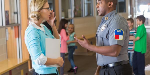 Security officer talking to a teacher in a school hallway.