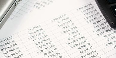 Pen and calculator on financial documents with numbers and figures.
