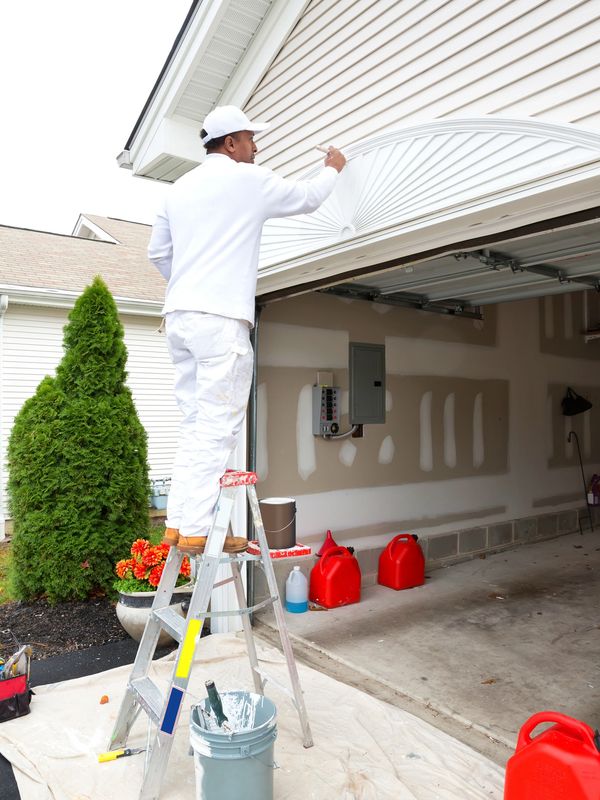 Painter working on a garage exterior from a ladder.