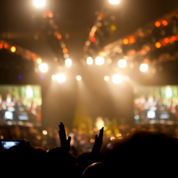 Blurry concert crowd with raised hands and bright stage lights.