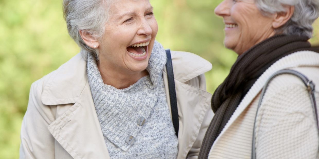 Two elderly women enjoying a cheerful conversation outdoors.