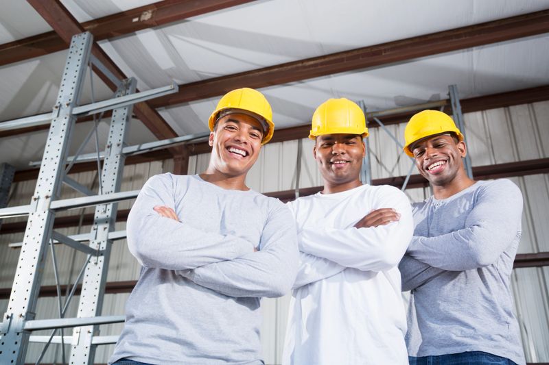 Multi-ethnic workers (20s, 30s) wearing hardhats, standing in warehouse.