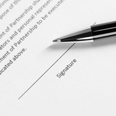 Pen poised to sign a document on the signature line.