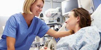 Nurse talking with a woman patient who is in a bed.