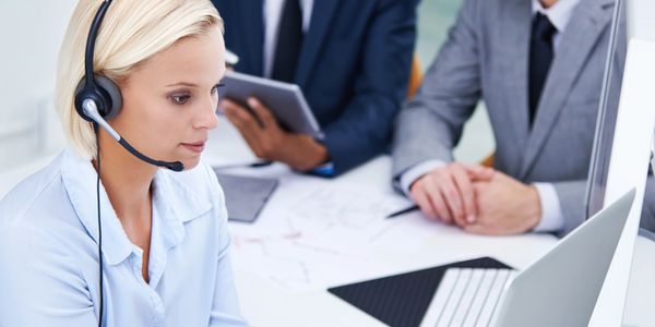 Customer service representative using a headset while colleagues discuss in the background.