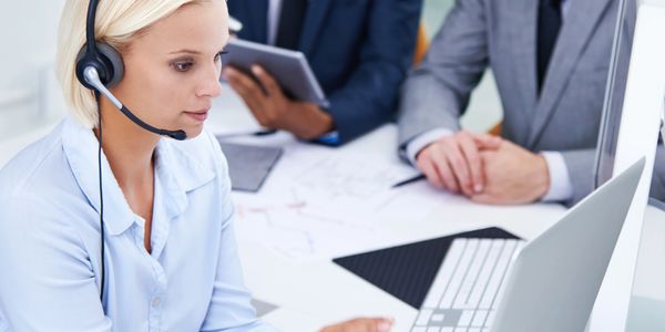 Customer service representative using a headset while colleagues discuss in the background.