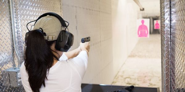Woman practicing shooting at an indoor gun range wearing ear protection.