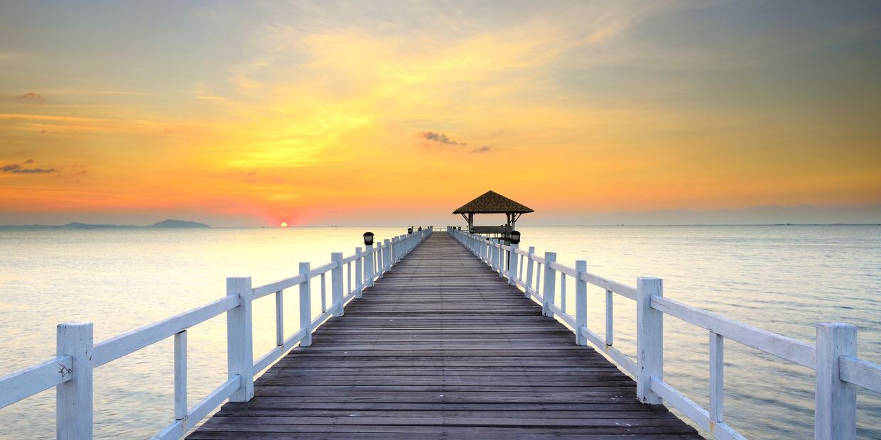Wooden pier extending into calm sea under a vibrant sunset sky.