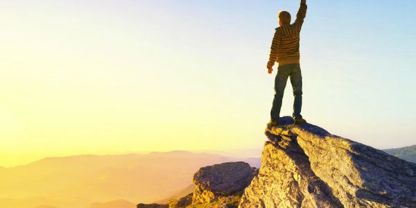 Person standing victoriously on a mountaintop at sunrise.