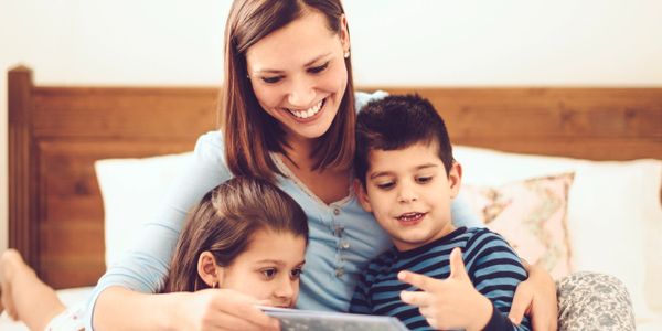 A mother reading a book with her two children on a bed, sharing a joyful moment.