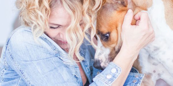 Woman with curly hair hugging a brown and white dog lovingly.