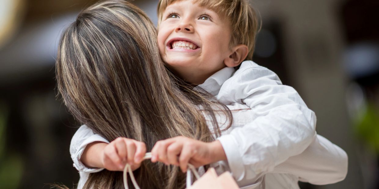 A joyful child hugging an adult with a big smile.