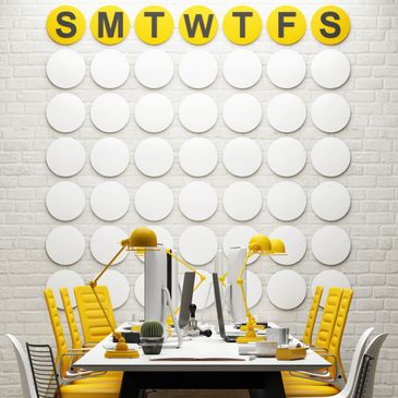 Modern office workspace with yellow chairs and lamps under a weekday wall calendar.