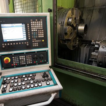 Industrial CNC machine with control panel and lathe chuck in a workshop.