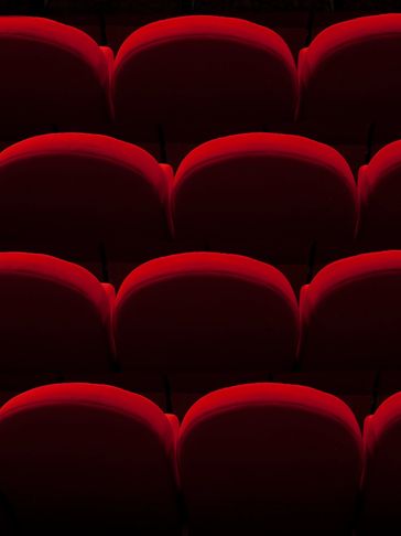 Rows of empty red theater seats in dim lighting.