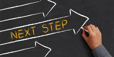 Hand drawing arrows and writing 'Next Step' on a blackboard.