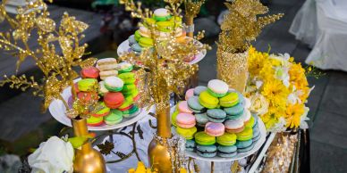 Colorful macarons displayed on decorative stands with gold accents and floral arrangements.