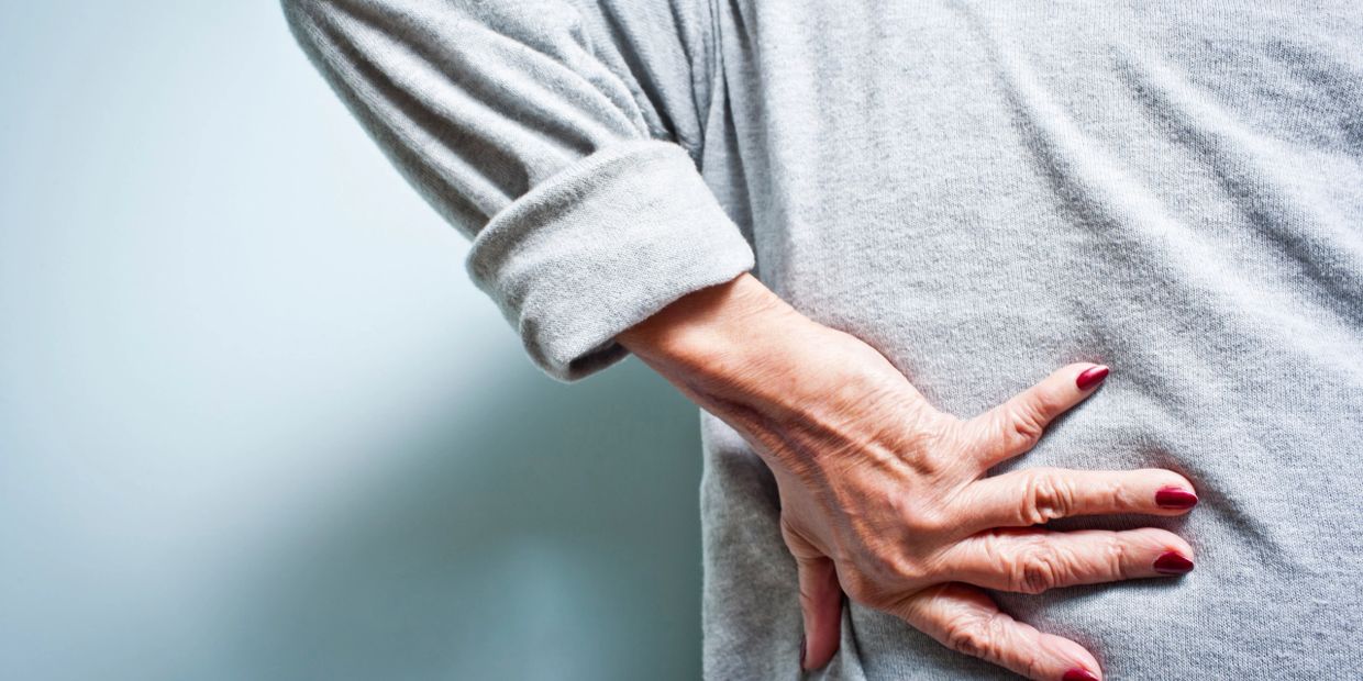 Person holding their lower back in pain, wearing a gray sweater.