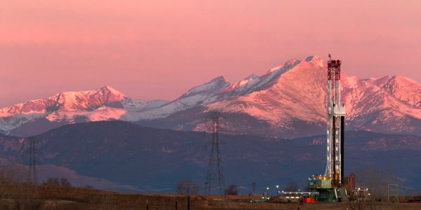 Oil drilling rig with snowy mountains at sunset.