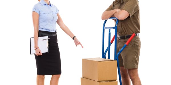 Woman pointing at stacked boxes on a hand truck with a smiling delivery man.