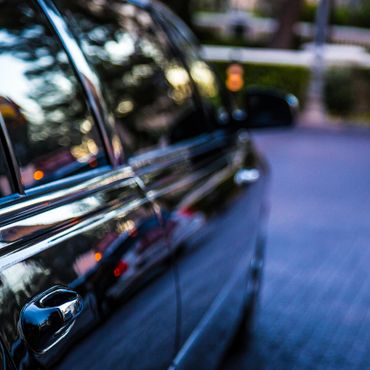 Close-up of a shiny black car door reflecting lights and surroundings.