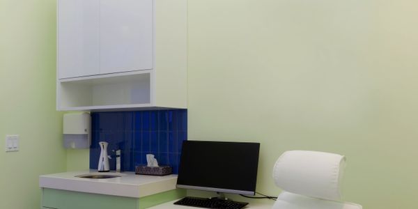 Minimalist office corner with computer, white chair, and sink area.