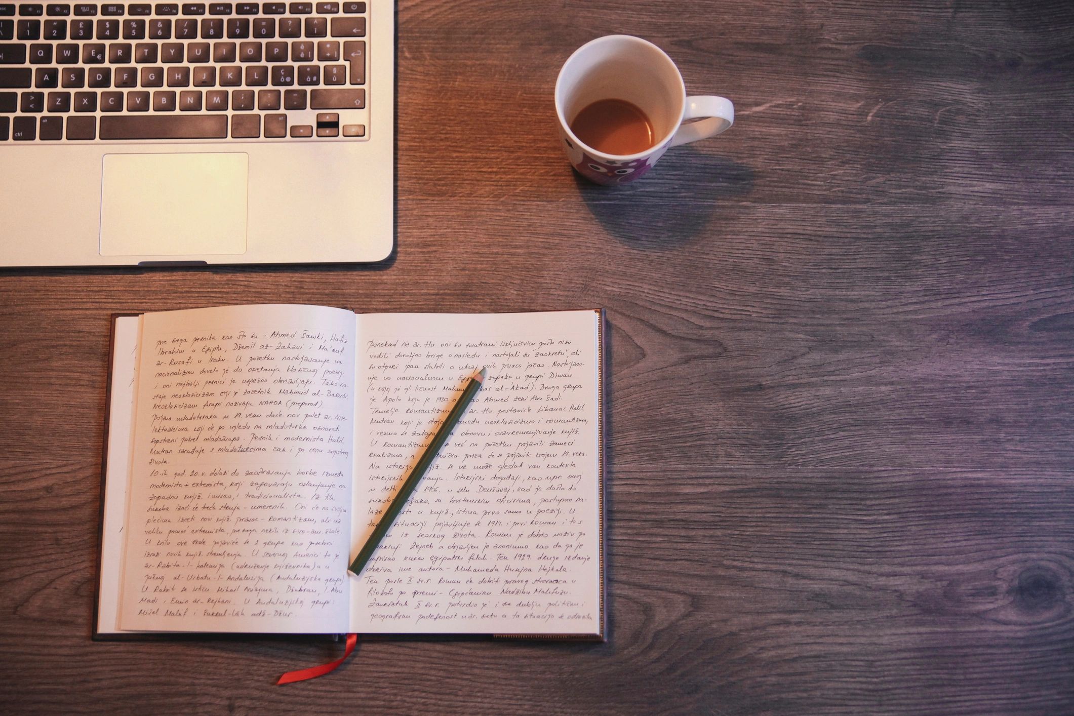 Open journal with handwritten notes, pencil, laptop, and coffee cup on a wooden desk.