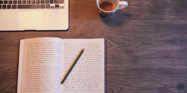 Notebook, pencil, laptop, and coffee on a wooden desk.