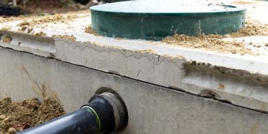 A pipe connected to a concrete septic tank with a green lid.