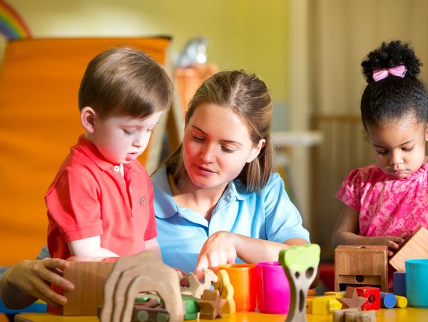 Teacher assisting young children with educational toys in a classroom.