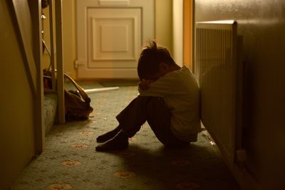 A child sitting alone on the floor, hugging knees, in a dimly lit hallway. rape definitions, sexual abuse, sexual assault, uk sexual offences