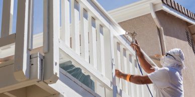 Person spray painting a white wooden balcony railing.