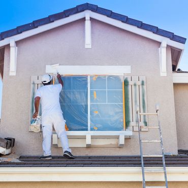 Painter applying white paint to a house exterior above a window.
