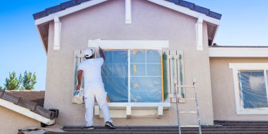 Painter working on a window frame outside a house.