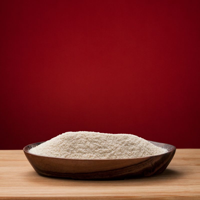 Grits is in wooden bowl which is on plank on red background 