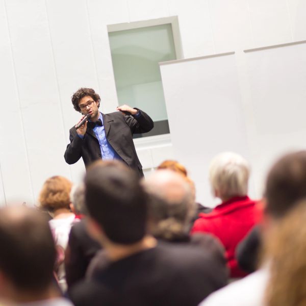 Man giving a speech to an audience using a microphone.