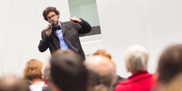 Man speaking passionately to an audience with a microphone.