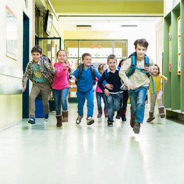 Group of happy children running in a school hallway with backpacks.