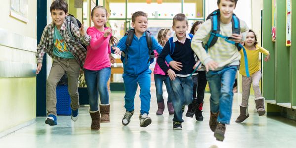 Happy children running joyfully down a school hallway with backpacks.