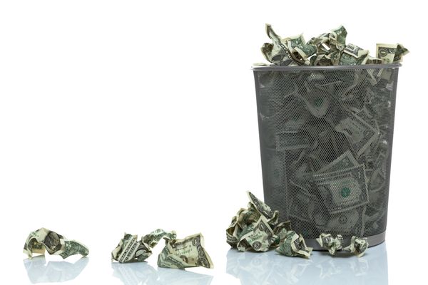 Crumpled dollar bills overflowing from a trash bin.