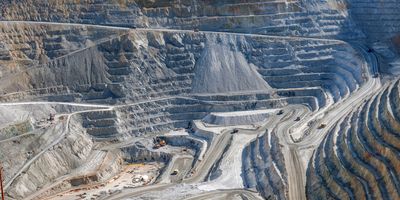 Open-pit mining operation with stepped terrain, haul roads, and heavy machinery extracting minerals.