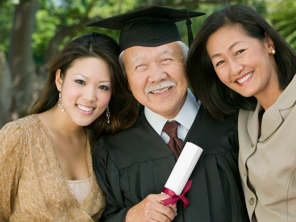 Elderly man in graduation gown with two women smiling.