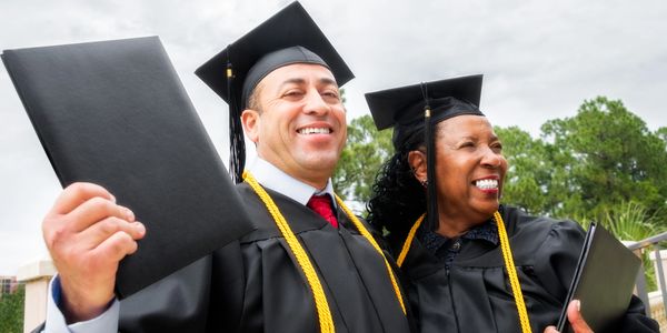 Two graduates smiling with diplomas and caps.