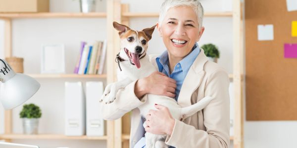 Smiling woman in office holding a happy dog on her lap.
